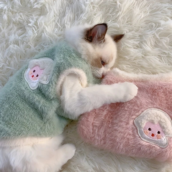 Cat in a green outfit with butterfly wings lying on a fluffy white surface.